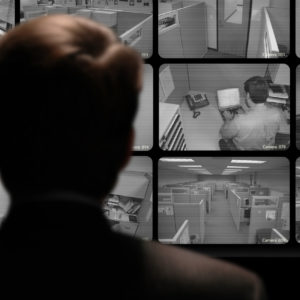 Man watching an employee work via a closed-circuit video monitor
